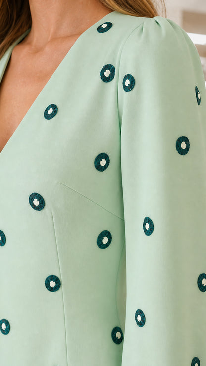 Close-up detail of mint green dress showing V-neckline and textured circular embroidery