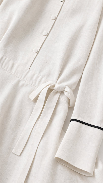 Close-up detail of button placket, cuffs, and waist tie on white dress
