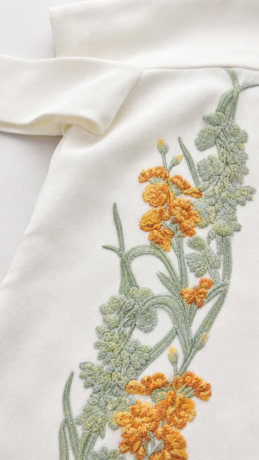 Close-up detail of yellow and green floral embroidery on white fabric