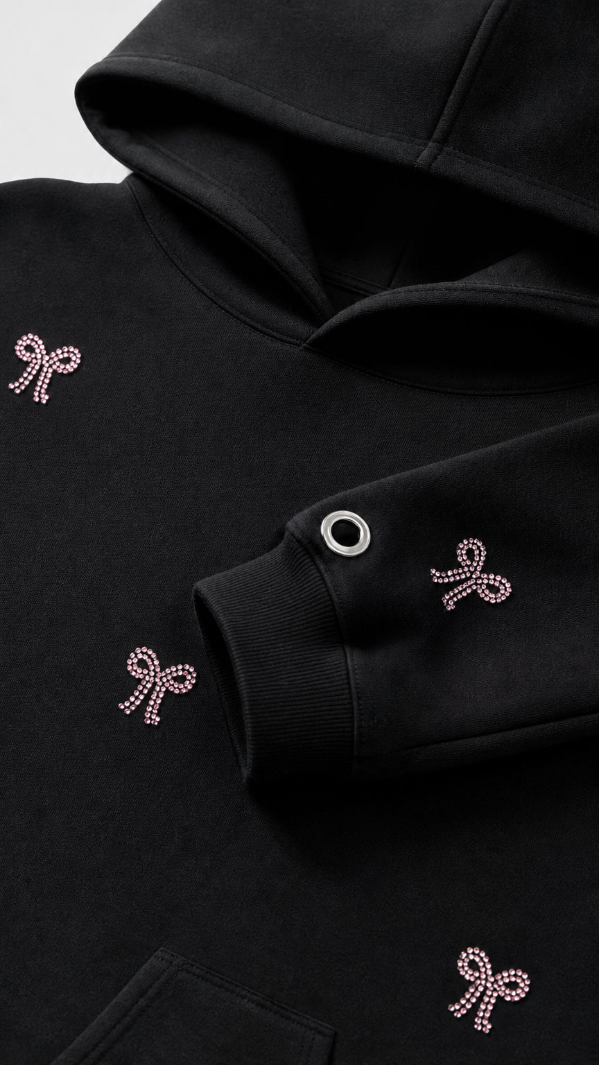 Close-up detail of rhinestone bow embellishments and sleeve grommet on black hoodie