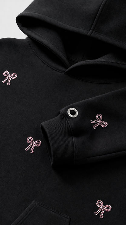 Close-up detail of rhinestone bow embellishments and sleeve grommet on black hoodie