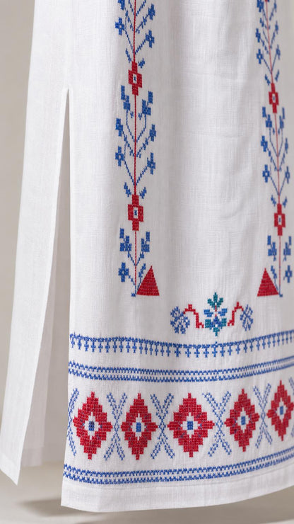 Close-up detail of blue and red geometric embroidery and side slit on white dress