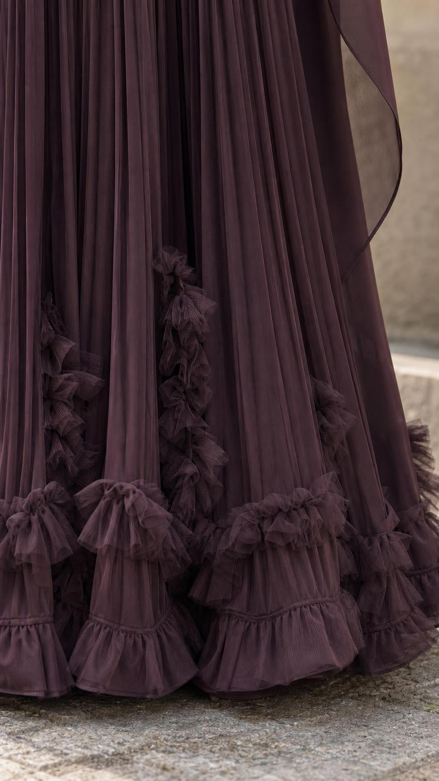 Close-up detail of ruffled hem and pleats on plum maxi dress