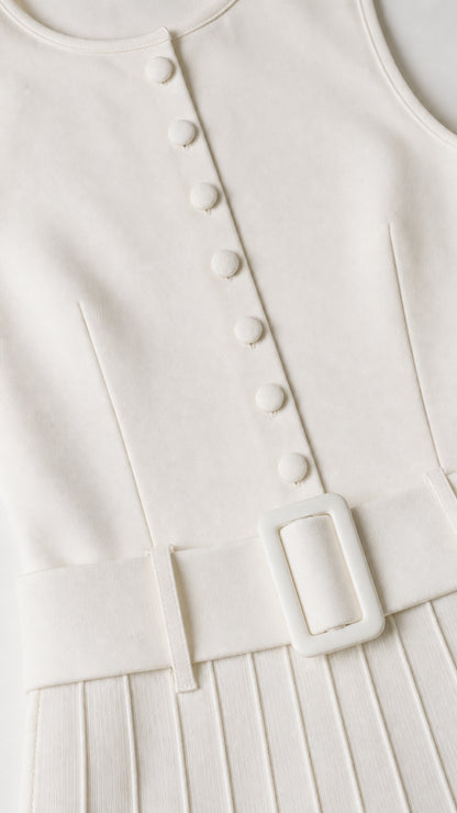 Close-up detail of covered buttons, belt buckle, and pleats on white dress