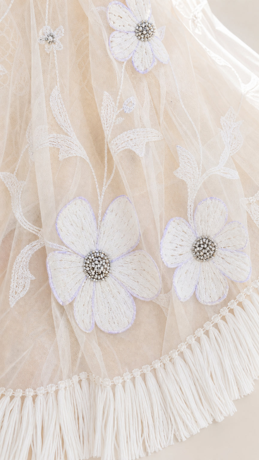 Close-up detail of white mesh fabric with floral embroidery and tassel fringe
