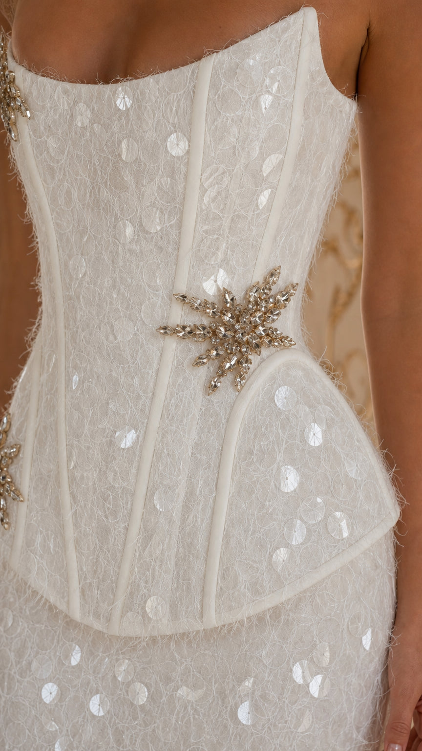Close-up detail of white sequin corset bodice, boning lines, and crystal starburst brooch