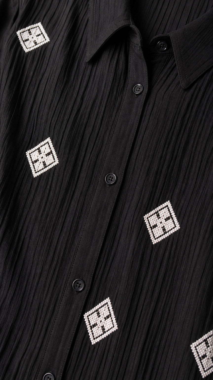 Close-up detail of textured crinkle black fabric with geometric square embroidery and buttons