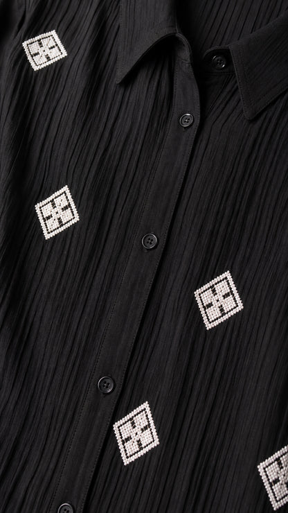 Close-up detail of textured crinkle black fabric with geometric square embroidery and buttons