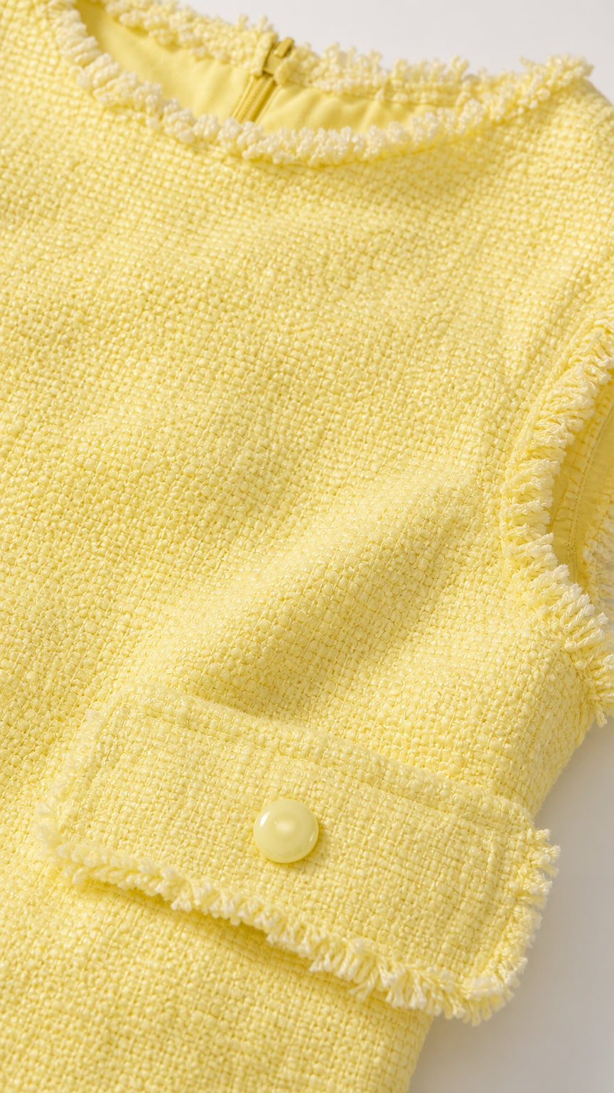 Close up of yellow tweed fabric, fringe trim, and pocket detail