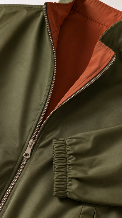 Close-up detail of the olive green jacket with metal zipper, contrast orange lining, and elastic cuff