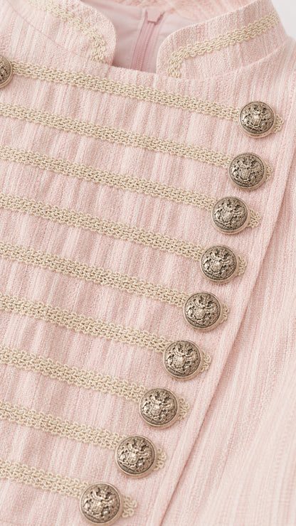 Close-up detail of textured fabric, braided frogging, and embossed crest buttons in blush pink