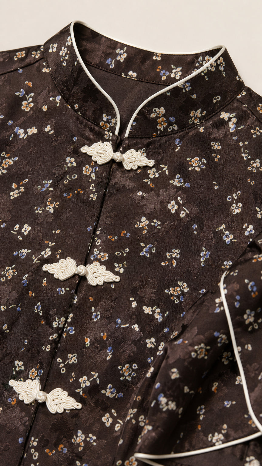 Close-up of Mandarin collar, white piping, and frog closures on dark brown floral fabric