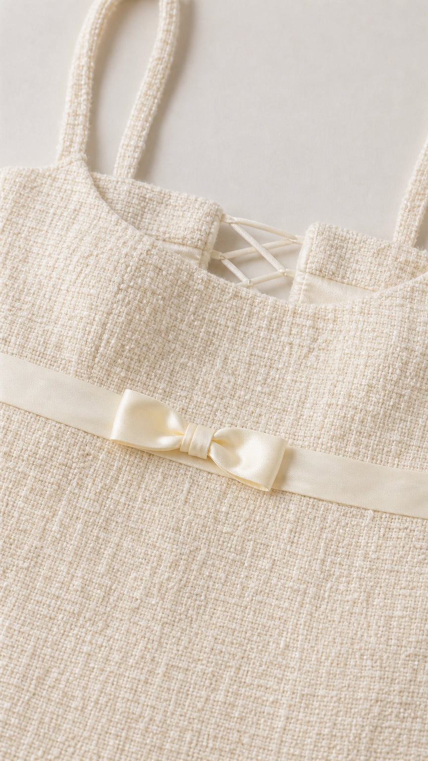 Close-up detail of cream tweed fabric, satin bow, and back lacing