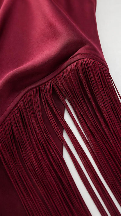 Close-up detail of smooth satin fabric and fringe hem in burgundy