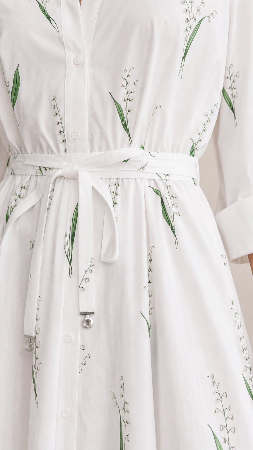 Close-up detail of fabric, belt, and botanical print on white dress