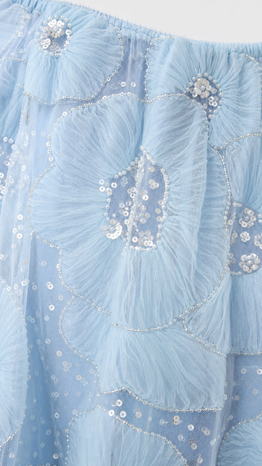 Close-up detail of tulle floral appliqués and sequins on light blue dress
