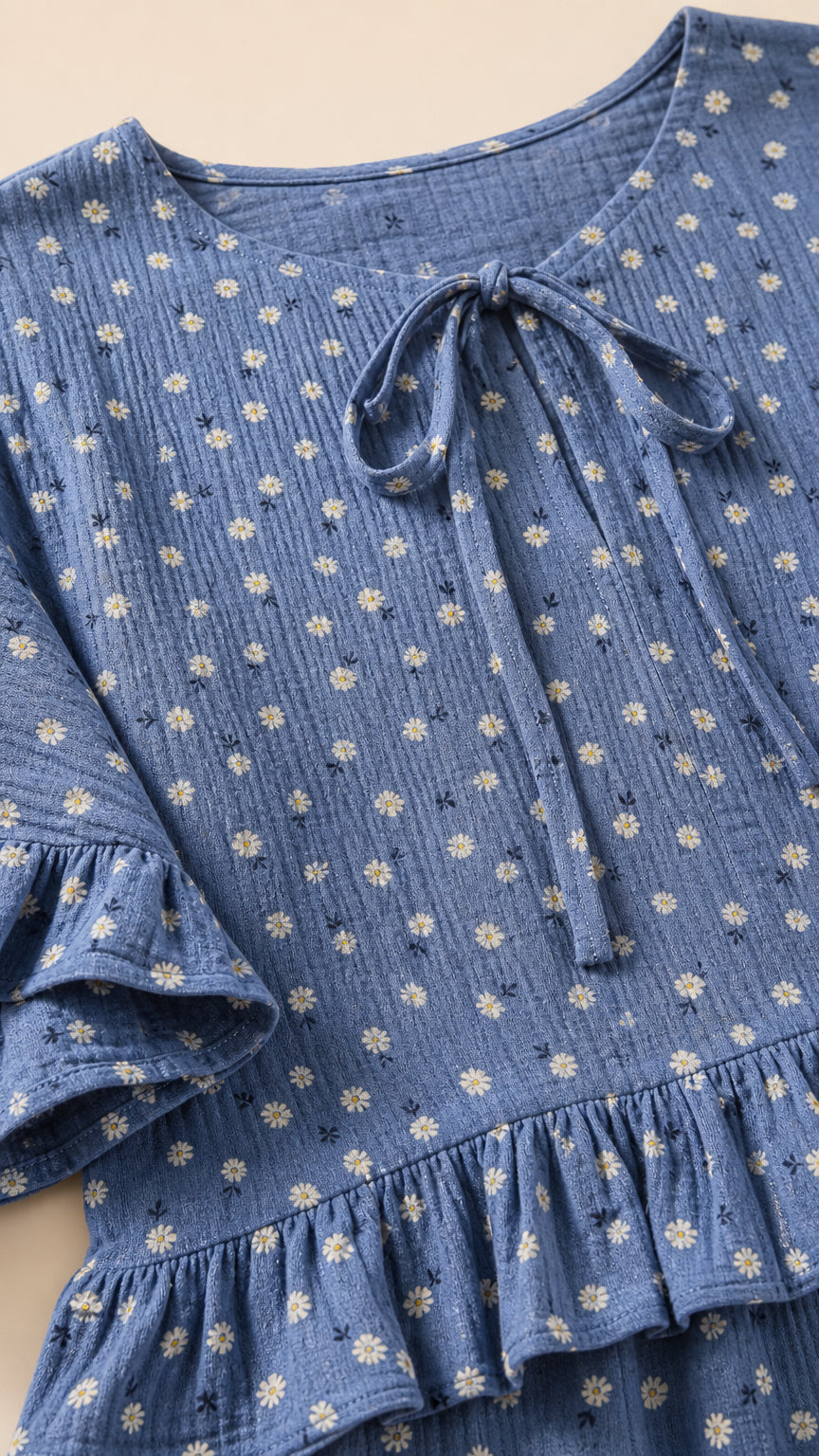 Close-up detail of blue textured floral fabric, front tie neck, and ruffle hem