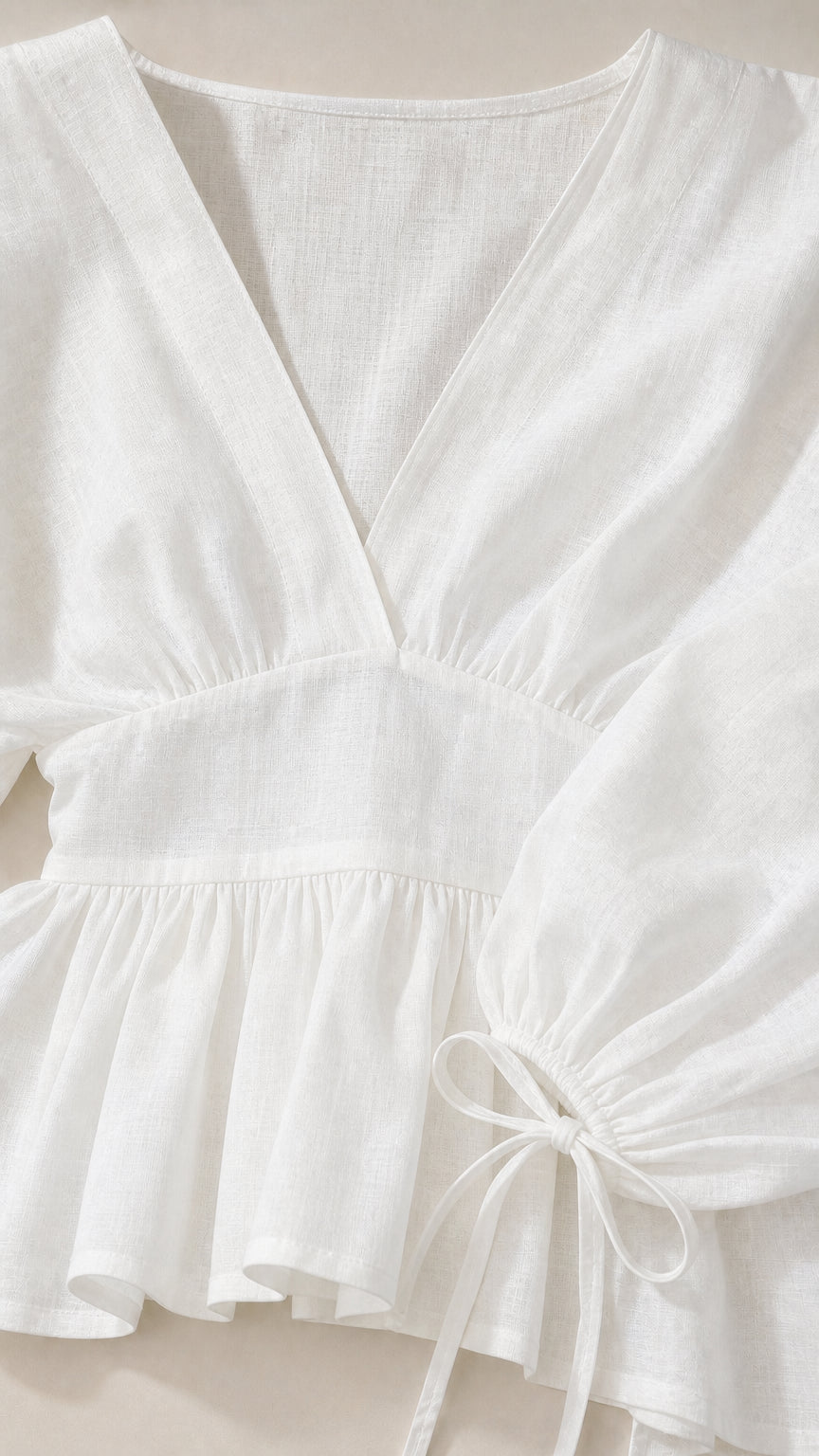 Close-up detail of white V-neckline, peplum waist, and tie cuff