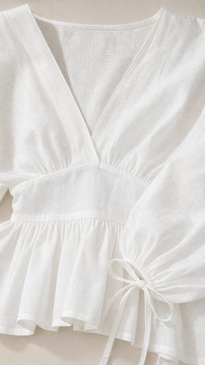 Close-up detail of white V-neckline, peplum waist, and tie cuff