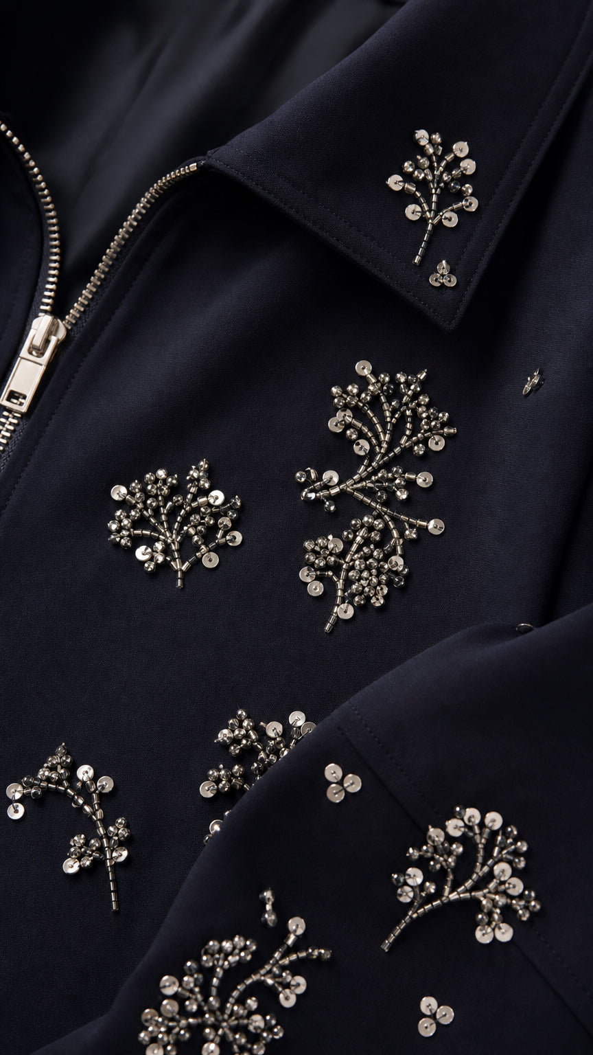 Close-up detail of silver beaded floral embroidery and zipper on navy jacket
