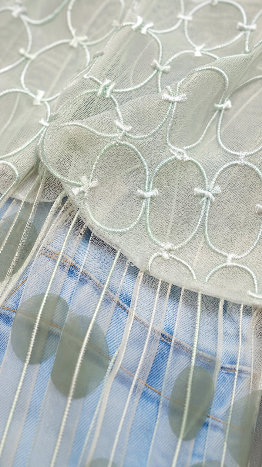Close up of sage sheer mesh fabric with embroidery and fringe