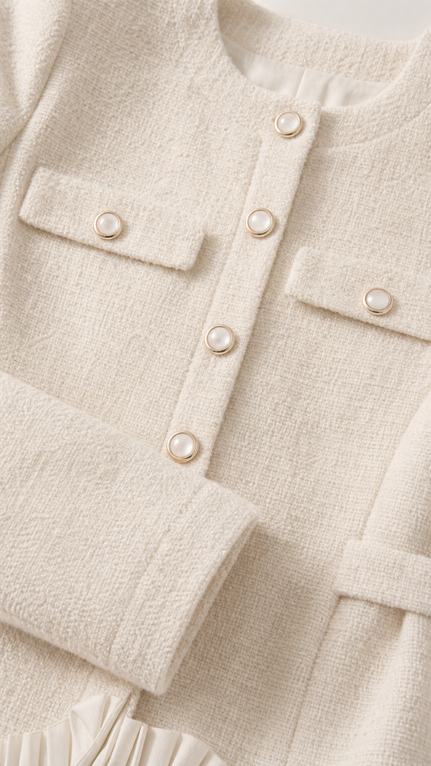 Close-up detail of textured cream tweed fabric, buttons, chest pockets, and pleated trim