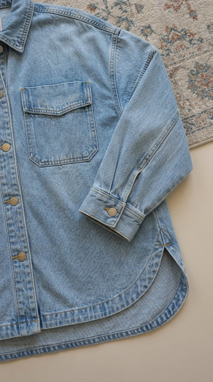 Close-up detail of pocket, sleeve cuff, and curved hem on light blue denim fabric