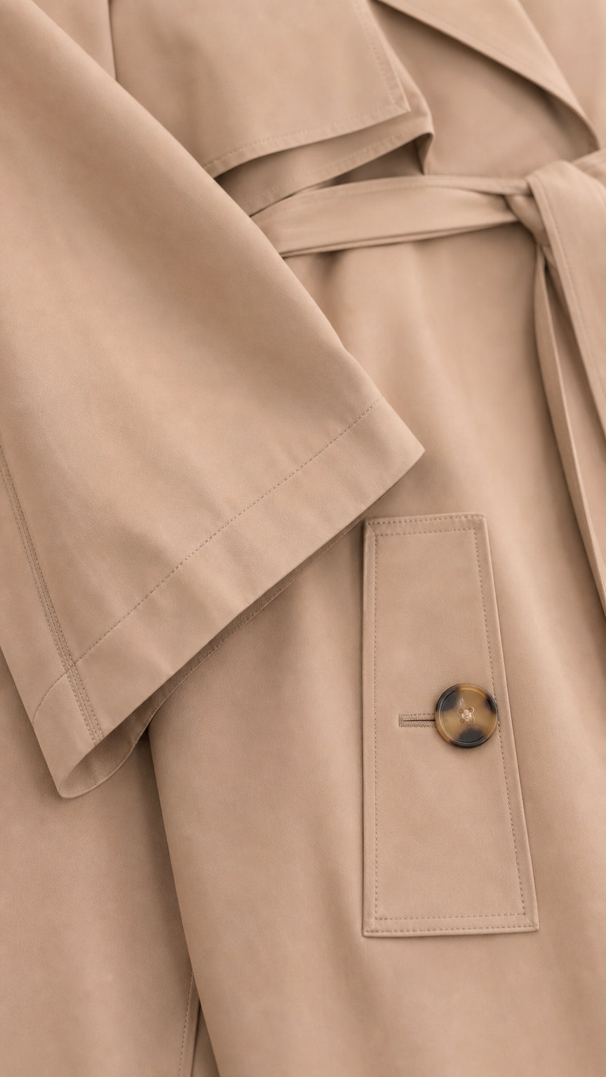 Close-up detail of smooth Camel outerwear fabric, tie belt, and buttoned pocket