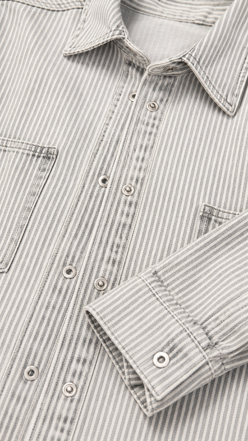Close-up detail of striped denim fabric showing collar, snap buttons, and chest pocket