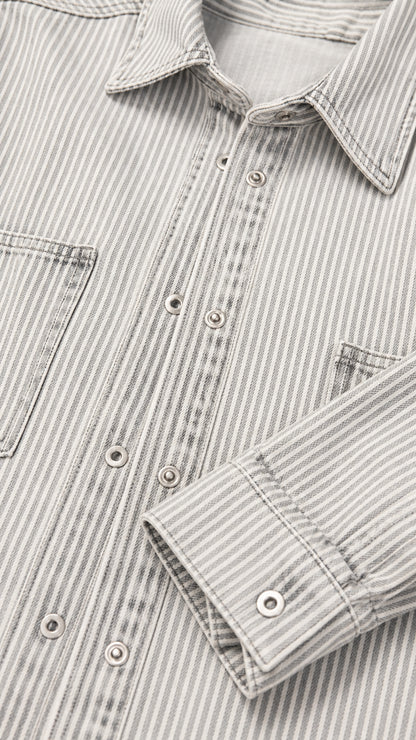 Close-up detail of striped denim fabric showing collar, snap buttons, and chest pocket