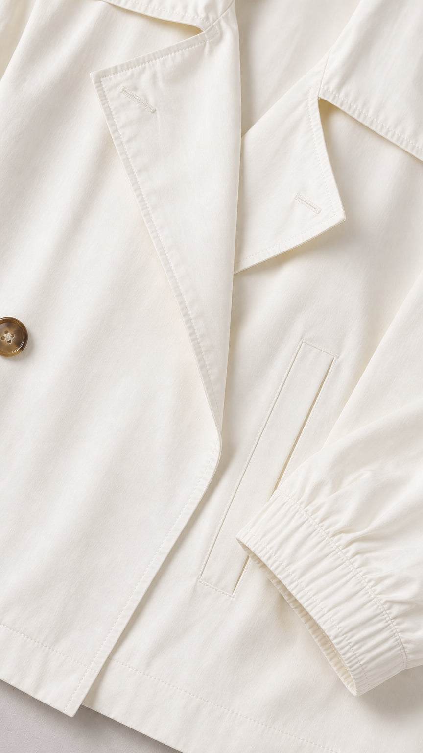 Close-up of the white blazer lapel, front button, pocket, and elastic cuff details