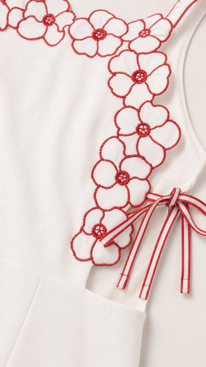 Close-up detail of red floral embroidery and ribbon tie on white fabric