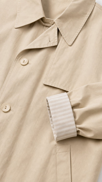 Close-up detail of collar, buttons, and striped cuff lining on beige trench coat