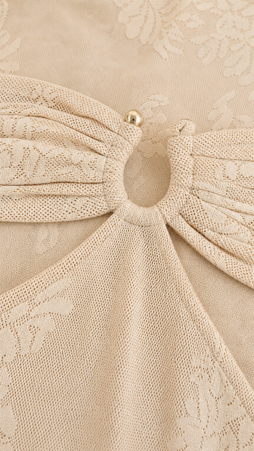 Close-up detail of center ring hardware and textured knit fabric on beige dress
