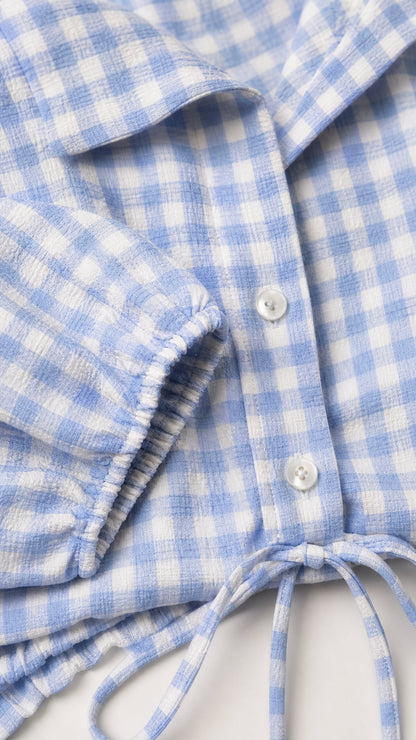 Close-up detail of light blue gingham check fabric, collar, and button placket