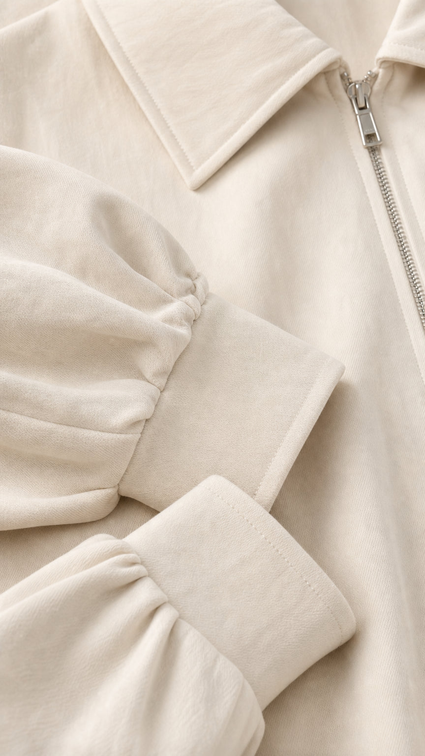 Close-up detail of cream jacket collar, metallic zipper, and gathered cuff