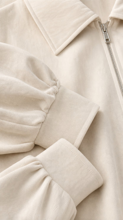 Close-up detail of cream jacket collar, metallic zipper, and gathered cuff