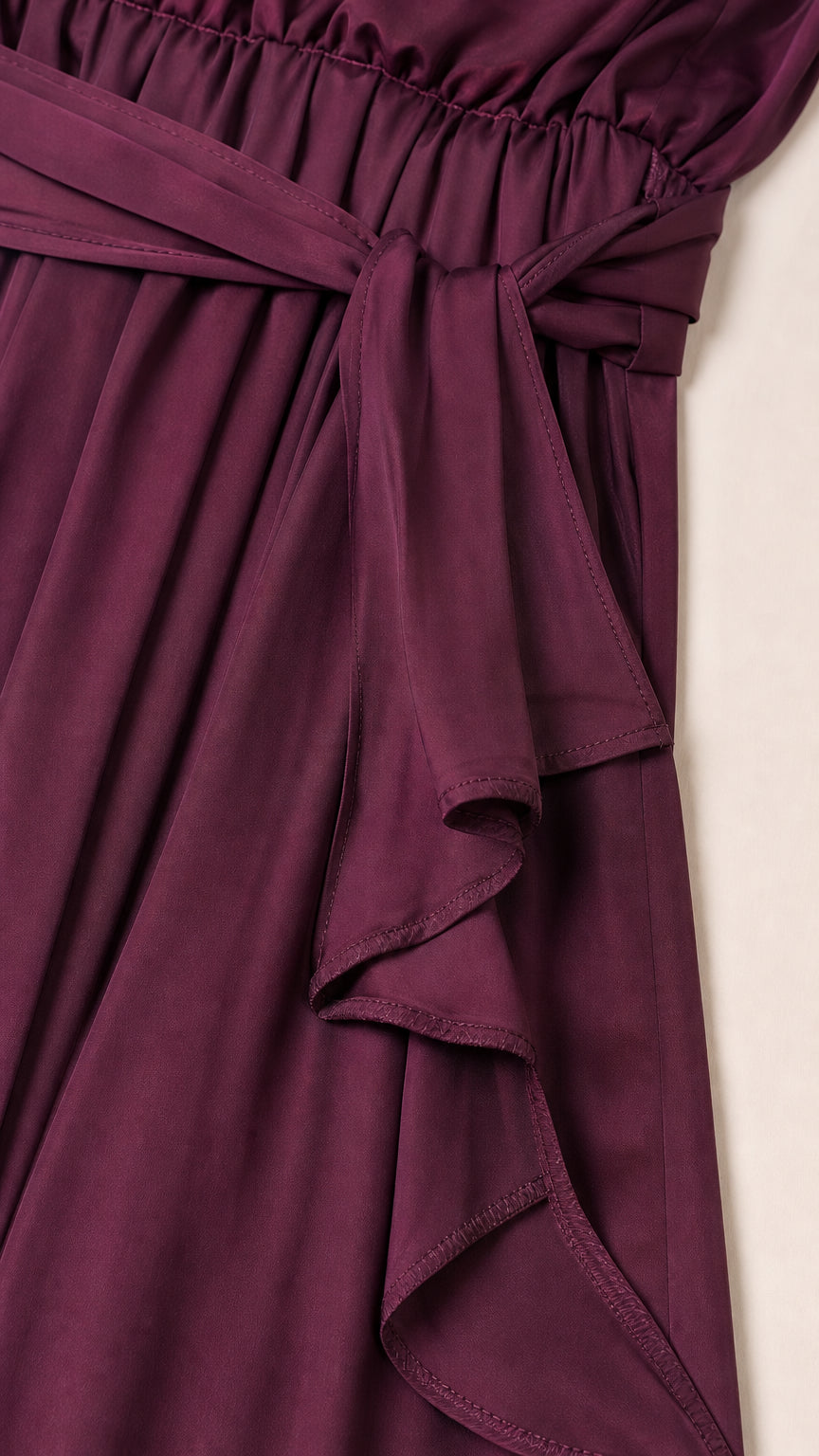 Close-up of the burgundy jumpsuit waist tie and layered side drape detail