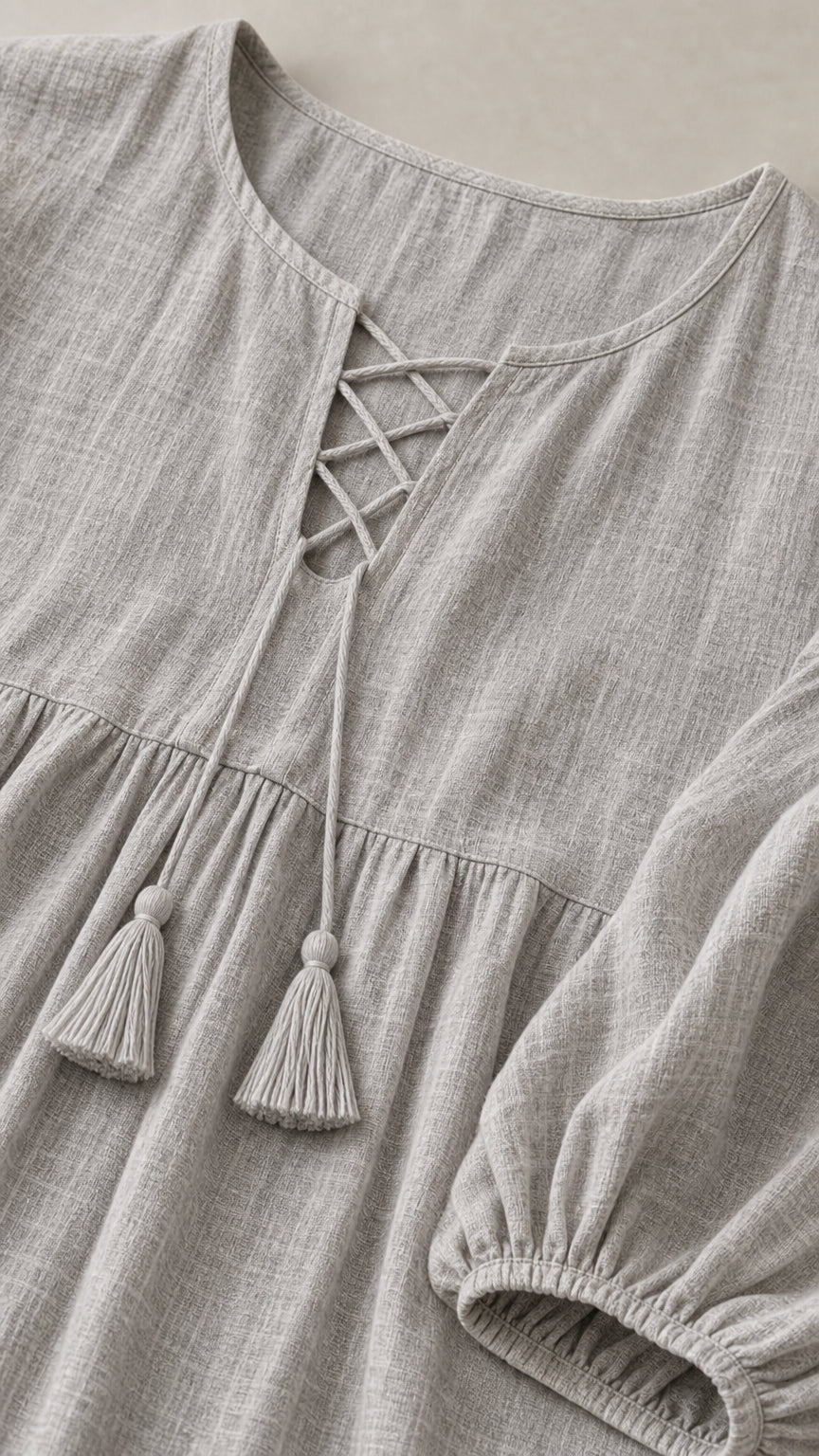 Close-up detail of grey textured fabric, lace-up split neckline, and tassel ties