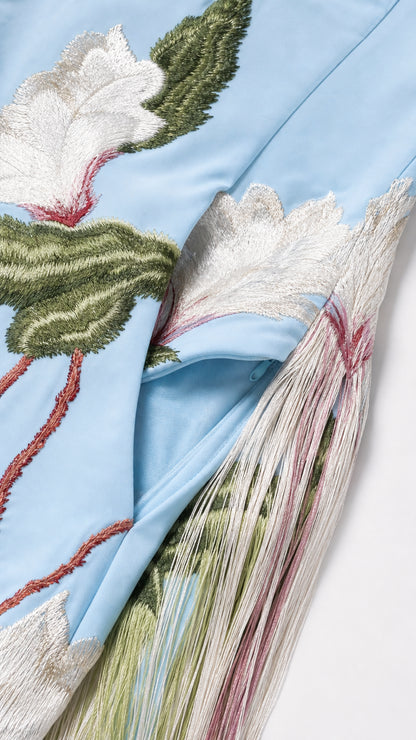 Close-up of intricate white floral embroidery and multi-colored fringe hem on Light Blue fabric