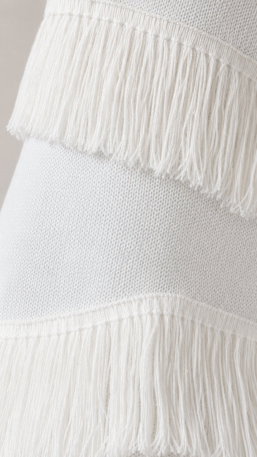Close-up detail of textured knit fabric and tiered fringe on white skirt