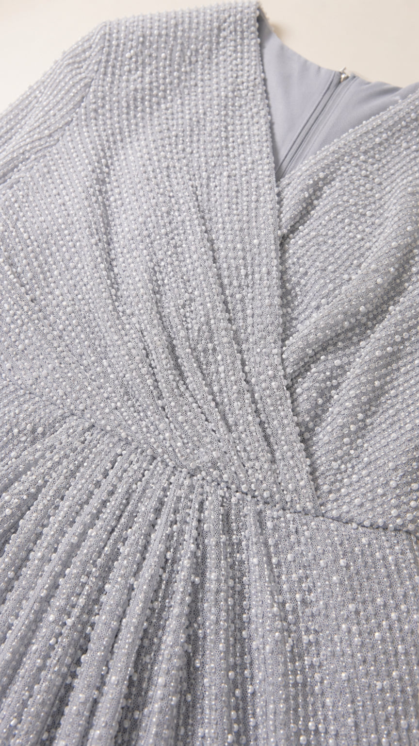 Close-up detail of Silver shimmer pleated fabric, V-neckline, and back zipper construction