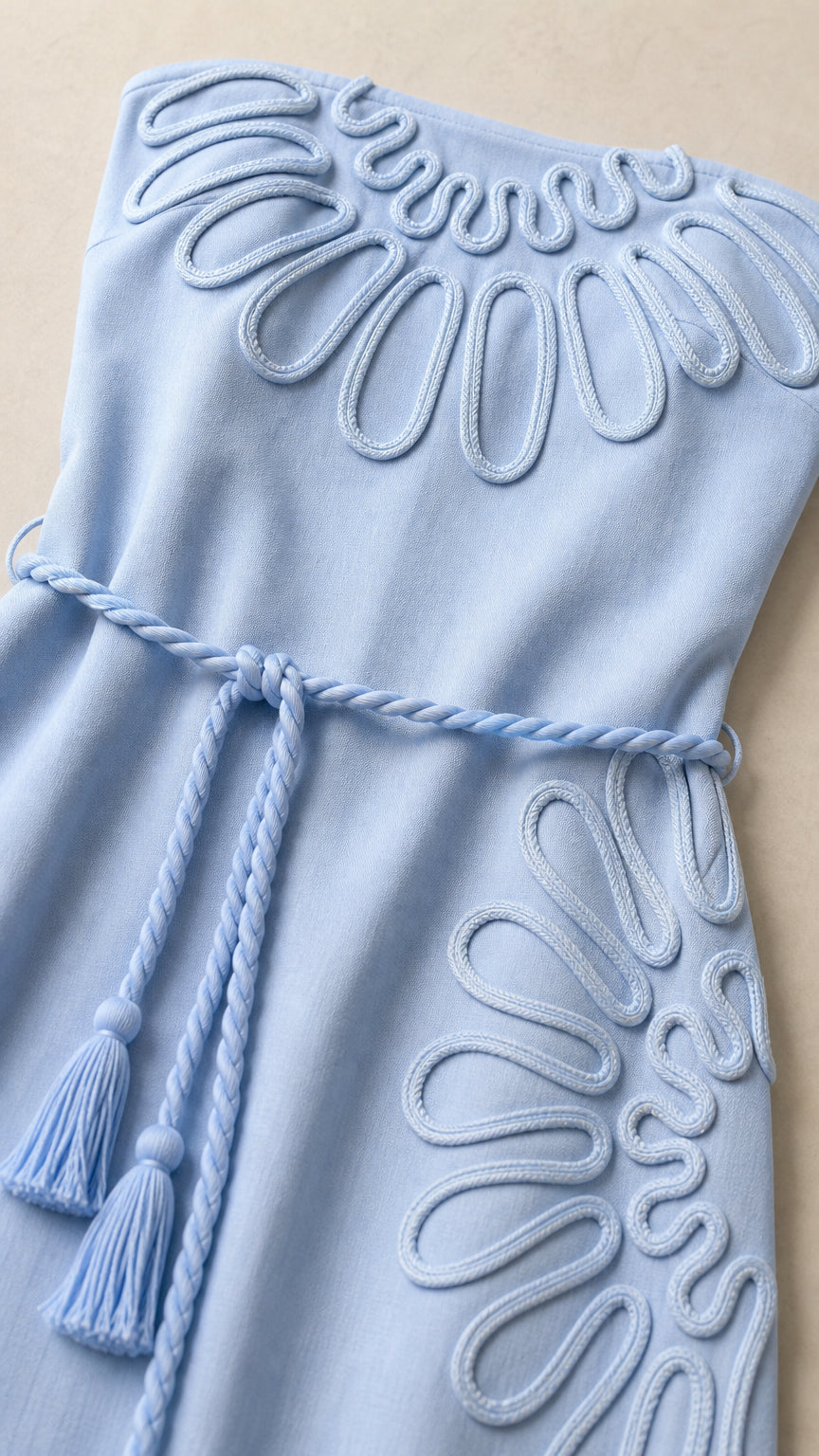Close-up of floral cord embroidery and braided belt on light blue dress
