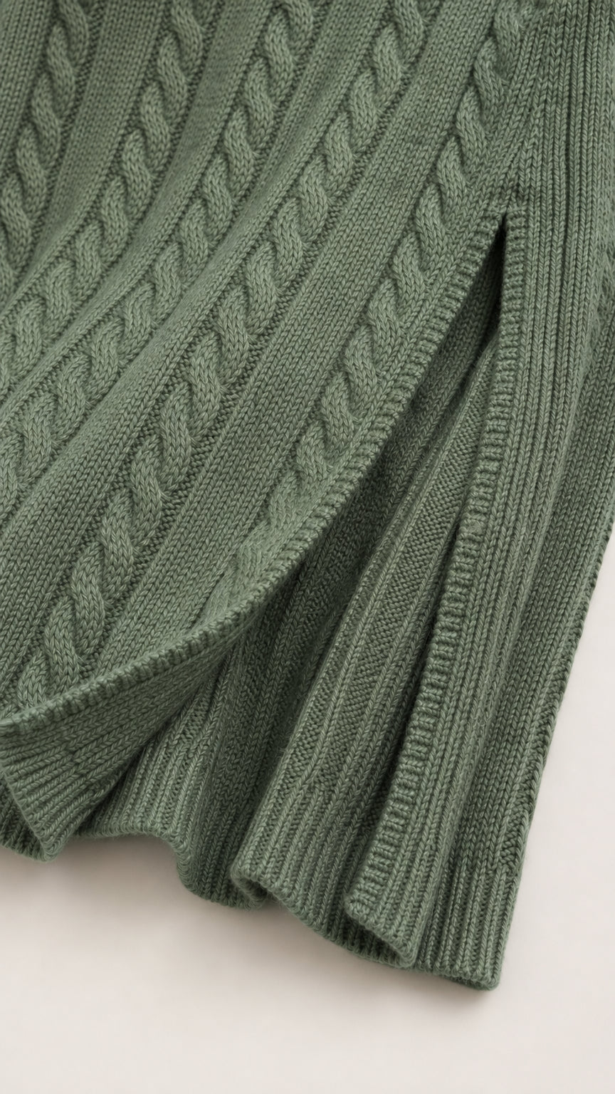 Close-up detail of green cable knit texture, ribbed hem, and front slit