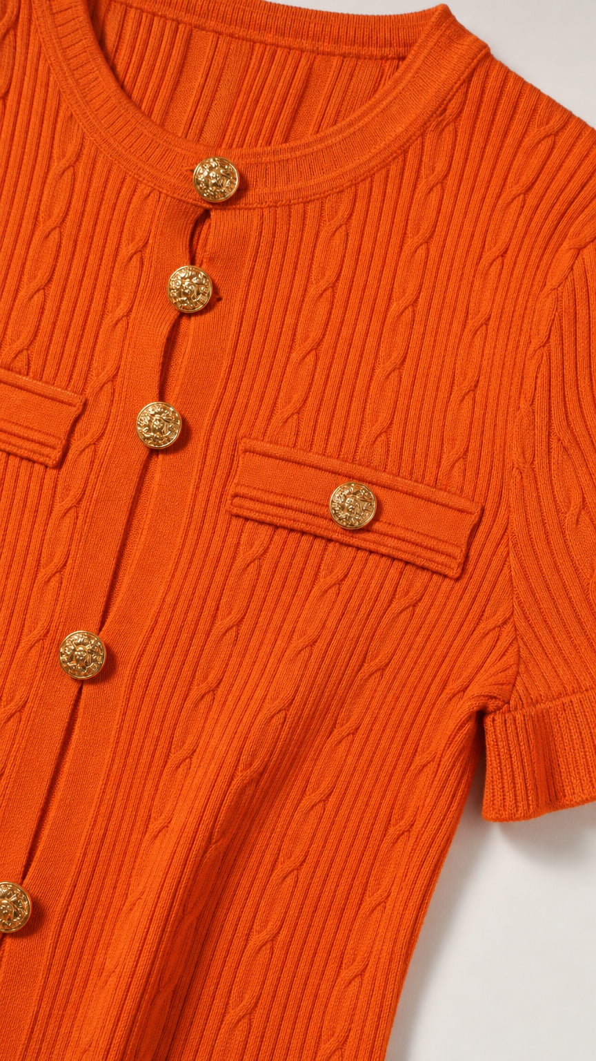 Close-up detail of orange cable knit texture, round neckline, and embossed gold-tone buttons