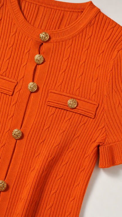 Close-up detail of orange cable knit texture, round neckline, and embossed gold-tone buttons