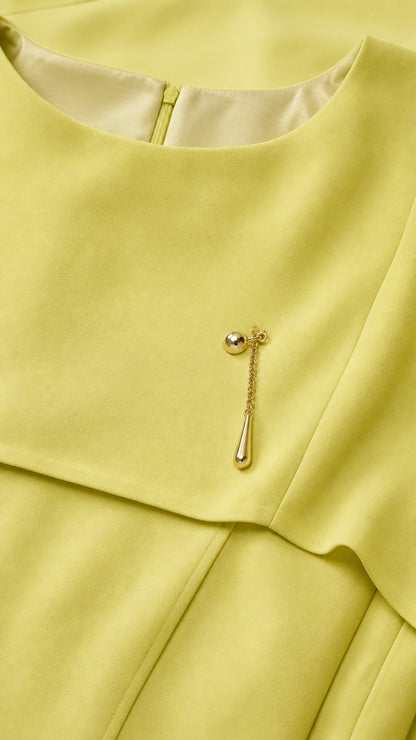 Close-up of boat neckline and gold brooch pin detail on yellow gown