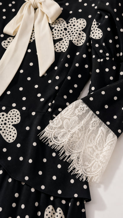 Close-up detail of cream neck bow and white eyelash lace cuffs on black polka dot dress