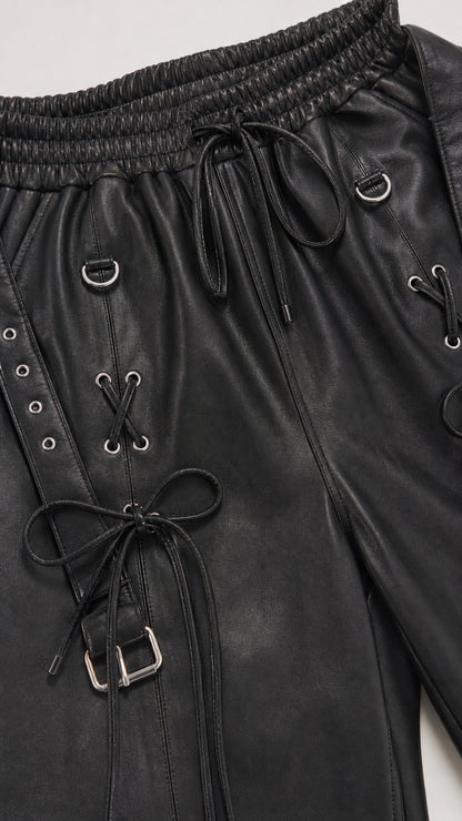 Close-up of black faux leather jogger pants with lace-up details and hardware