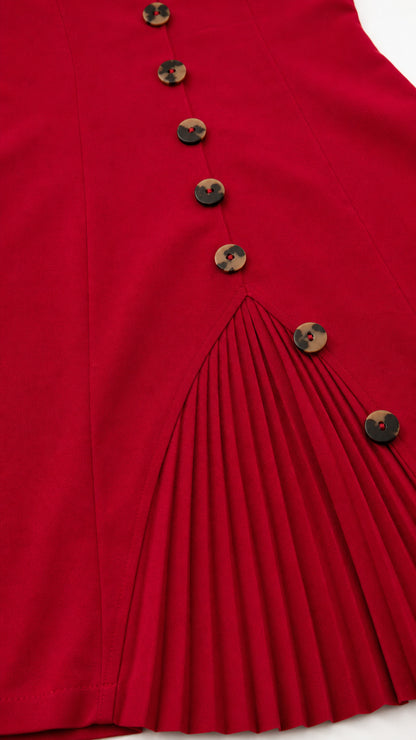 Close-up detail of tortoiseshell buttons and sharp knife pleats on the red dress hem
